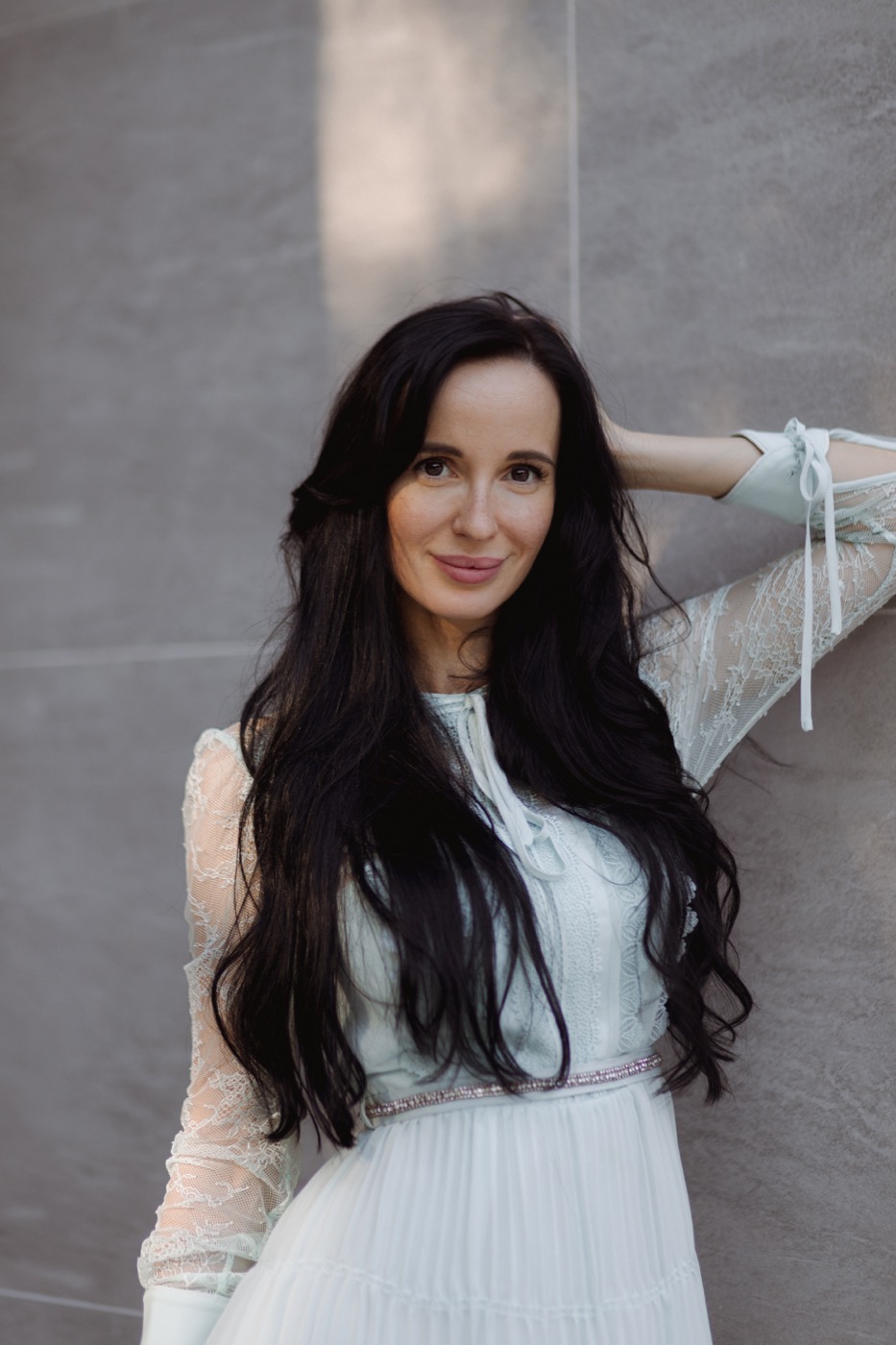 Close portrait of Anna Shatkovskyy in a white dress against a modern architectural wall.